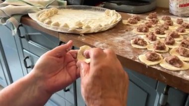 Mavi bluzlu ve beyaz eşarplı bir büyükanne torun için turta ve diğer hamurlardan pişirir. Hamuru yoğurur. Gülümser ve ev yapımı ürünlerin reklamını yapmaktan mutluluk duyar.