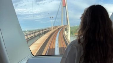 Sarışın, beyaz tişörtlü, gökyüzü trenine binen Avrupalı bir kız sırtı kameraya dönük duruyor ve trenin ön camına bakıyor başka bir hava treni Vancouver Kanada 'da ilerliyor.