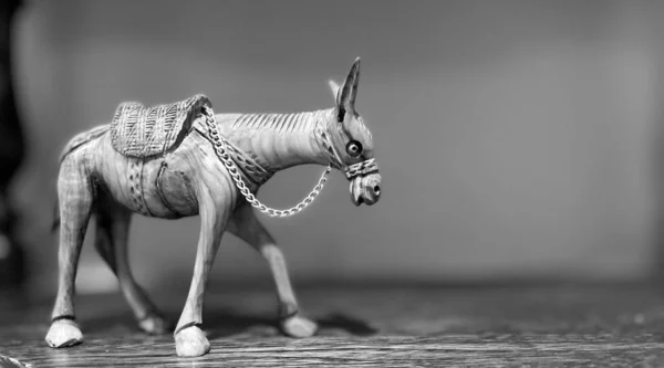 A black and white figurine of a wooden donkey who lowered his head on a chain he stands on a wooden one on a black and white surface. High quality photo