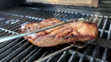 Ateşin üstünde kocaman bir parça et mutfak maşasıyla çevirilir. Çok güzel kokar ve lezzetlidir. Izgaranın şeritleri siyahtır ve henüz hazır değildir.