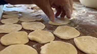 Büyükannem torunu için lezzetli börekler, turtalar ya da börekler hazırlar. Hamuru sallar, parçalara ayırır ve masanın üzerinde heykeller yapar. Üzerinde un serpiştirilmiş hamurlar vardır.