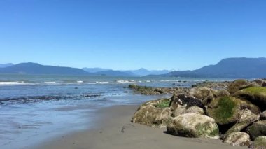 Kamera Pasifik Okyanusu 'nun kıyılarını göstermek için yavaşça döner. Dev taşların sağ tarafından gökyüzünün mavi suyunu görebilirsiniz. Wreck Sahili, Tower Sahili, Acadia Sahili Çıplaklar Plajı Vancouver