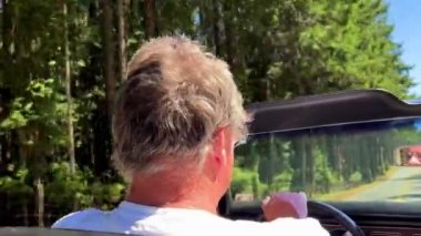 a man driving a convertible rides in the forest on the road he has gray hair he is 60 years old travel travel by car . High quality photo