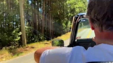 a man driving a convertible rides in the forest on the road he has gray hair he is 60 years old travel travel by car . High quality photo