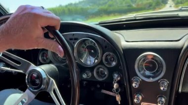 An old retro car Corvette is driving along road a man holds his hand on the steering wheel a middle-aged man a hand with a ring is visible a little mostly the steering wheel Vancouver Canada 07.2022