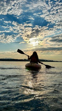 a teenage girl is kayaking at sunset in the Pacific Ocean, only the silhouette of Kayak and Paddles is visible she swims along a sunny path to the sea. a beautiful sky with small clouds