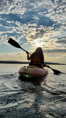 a teenage girl is kayaking at sunset in the Pacific Ocean, only the silhouette of Kayak and Paddles is visible she swims along a sunny path to the sea. a beautiful sky with small clouds