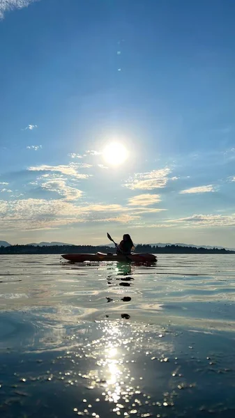 a teenage girl is kayaking at sunset in the Pacific Ocean, only the silhouette of Kayak and Paddles is visible she swims along a sunny path to the sea. a beautiful sky with small clouds