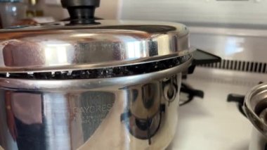 Stainless steel saucepan on stove, potatoes are boiled in it and steam comes out The water boils and huge bubbles appear that do not burst, crawling out from under the lid and inflate in full steam