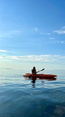 a teenage girl is kayaking at sunset in Pacific Ocean, only the silhouette of Kayak and Paddles is visible she swims along a sunny path to the sea. a beautiful sky with small clouds 08.2022 Canada 
