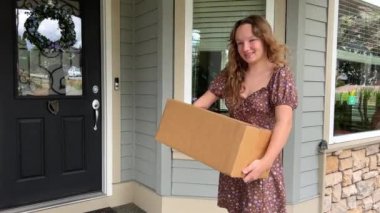 A girl in her hands with a cardboard box stands near the door of a private house and smiles looks into the frame Her hair develops in the wind She brought home delivery to the door
