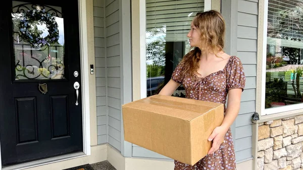 A teenage girl looks in surprise at the box that stands on her porch, she crossed her arms over her chest and is surprised at her long blond hair She doesnt remember ordering delivery