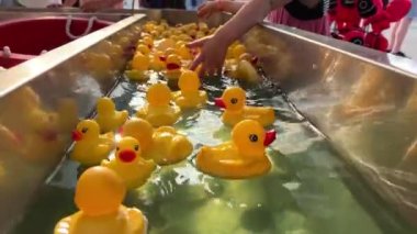 Rubber children ducks swim on the water there are a lot of them they swim one after another each bright yellow with a red beak They follow the flow of water directly to the camera as they swim past