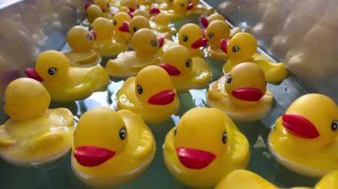 Rubber children ducks swim on the water there are a lot of them they swim one after another each bright yellow with a red beak They follow the flow of water directly to the camera as they swim past