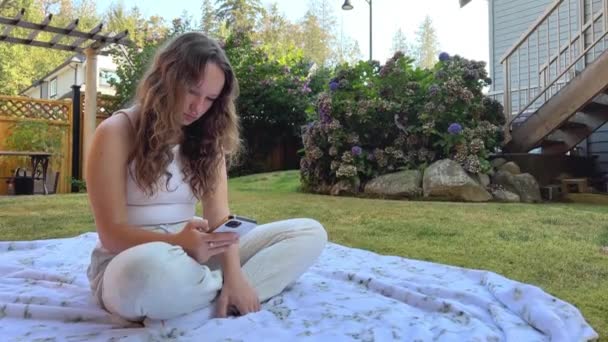 European Girl Siedzi Polanie Białym Kocu Białych Ubraniach Rękach Telefonem — Wideo stockowe