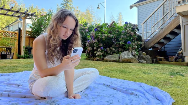 Social networks online learning is integral part of the life of schoolchildren high school students, teenagers. A girl is sitting on the phone in nature on a white blanket in white clothes In phone