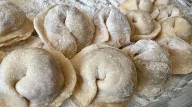  Hamur köftelerini heykeller ve ahşap bir masaya koyar, onlardan bir sürü vardır, unu iştah açıcıdırlar ve pişirilmeyi beklerler her hamur köftesi etle doludur, yuvarlaktır ve düzgünce el yapımıdır.