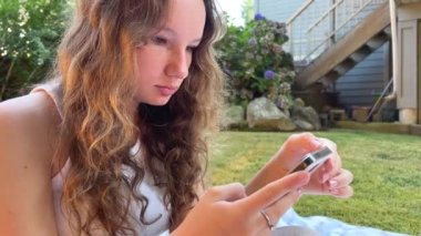 Beyaz bir çantada elinde telefonla oturan bir genç, gençlerin yoğun yaşamına ciddi şekilde odaklanmış bir şeye bakar. Dışarıda bir piknikte sosyal ağlarda ve gençlerle iletişim halinde.