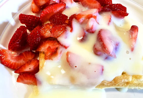 On waffles a lot of chopped strawberries drenched in pudding Custard with boiled egg yolks and homemade milk slowly drains from the waffle forming a puddle of delicious dessert strawberries cut