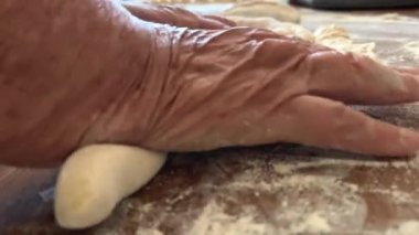 Yaşlı bir kadının yaşlı elleri hamuru yuvarlar ve bir şeyler pişirir ya da hamur köftelerini ya da hamur köftelerini ahşap bir yüzeyde kaynatır. Yüksek kalite 4k görüntü