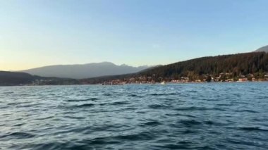 Limandaki karamsar Kordon Kordonu Ave Rocky Point Park Eğlence İskelesi Motorlu tekneden yavaş çekim kamera dalgaların üzerinden süzülüyor dağlar gökyüzü bulutsuz ve mavi okyanussuz açık mavi gökyüzü