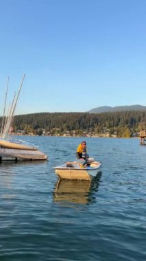 Kürek çeken bir kadın ve cankurtaran motorlu bir kurtarma botunda oturur ve ne yapılacağını gösterir. Kanada limanındaki Pasifik Okyanusu 'nda yüzer kasvetli Esplanade Ave Rocky Point Park İskelesi' nde