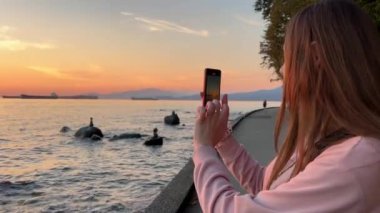 Neşeli genç kadın, Victorias Avustralya 'nın Büyük Okyanus Yolu' ndaki On İki Havari deniz taşlarının fotoğrafını çekiyor. Cep telefonuyla. Yüksek kalite 4k görüntü