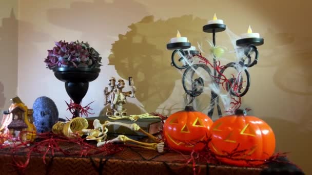 ハロウィンの装飾キャンドルスティックテーブルの上のすべての側面からクモの巣に包まれた2つのカボチャはそれに近くの黒い花瓶を点滅していますドライフラワーで二つの骨格は本の上に立ちます — ストック動画