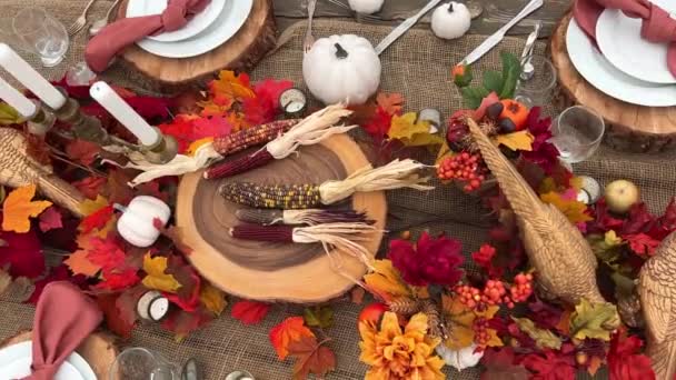 テーブルの上には木製のスタンドの横にプレートがありますフォークナイフと眼鏡赤いトウモロコシと黒いトウモロコシの乾燥した頭赤いナプキン真ん中にすべてがハロウィーンの秋の夜の夕食の準備ができています10月の夜 — ストック動画
