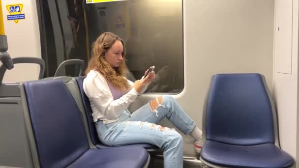 在温哥华 一个女孩坐在天窗旁边 没有人看得见她旁边唯一的蓝色空座位 她正在用电话看社交网络 — 图库视频影像