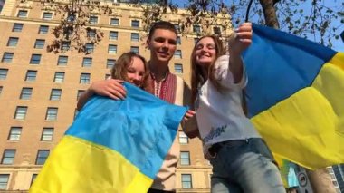 Ukrayna bayraklı iki kız, bir adam Ukrayna bayrağı sallayarak Ukrayna zafer bayrağı sarısı mavi flamalar üzerinde Ukraynalıların gücü ve iradesi kazanacak.
