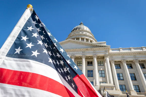 Ön planda bir Amerikan bayrağı var ve Salt Lake City 'deki Utah Eyalet Meclisi' nin ön tarafını kısmen kapatıyor.