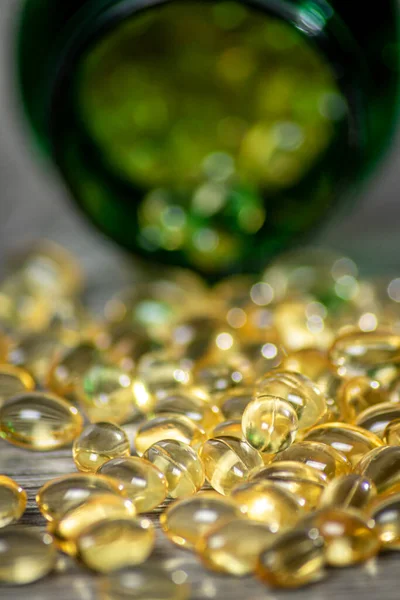 Yeşil bir vitamin jeli kapsülünün kapsülleri, sığ bir alan derinliğine sahip gri bir tahta tahtaya dökülmüş.