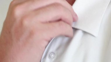 Beyaz gömleğin düğmelerini açan beyaz bir adam.