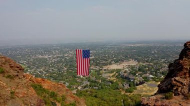 Drone Aerial Past American Flag Hanging Between Mountain Ridges into Valley With City