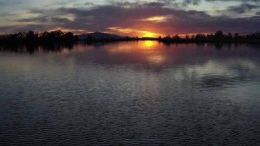 A Lake at Sunset With Cloudy Sunset Reflected in the Water Surface and a Fish Jumping Out of the Water