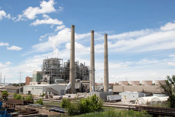 A power plant with several smoke stacks in the daytime with a blue sky
