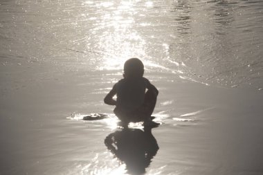 Küçük bir çocuk kumsalda bir şeyi inceliyor.