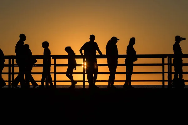 Silhouette of People Standing at a Railing With the Sun in the Background