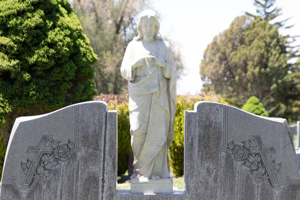 Stone statue of Jesus Christ pointing at His Sacred Heart on a headstone grave marker at a cemetery