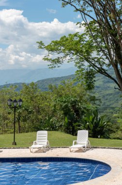 Havuzun yanındaki beyaz sandalyeler ve doğal manzara. Tamesis, Antioquia, Kolombiya.