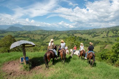 Tamesis, Antioquia, Kolombiya. 1 Temmuz 2018: Mavi gökyüzü ve dağlarla birlikte manzara. İnsanlar ata biniyor..