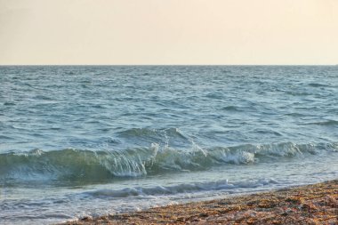 Güneşli bir yaz gününde gün batımında plaj. Sahilde deniz günbatımı manzarası. Deniz dalgası gün batımı renginde karaya çıktı. Batan güneşin ılık, yumuşak renklerinde. Dalgalar denize yuvarlanıyor.