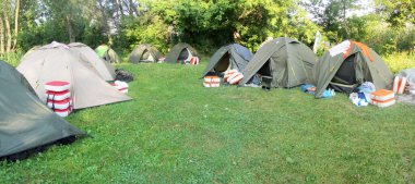 Birçok çadırın olduğu bir çadır şehri. Ormandaki yeşil çimlerin üzerinde. Etrafta bir sürü kamp malzemesi var. Bir kano gezisi sırasında bir gecelik ormanda kalan turist çadırları. Askeri kamp dinlenme yerinde.