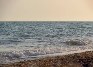 Güneşli bir yaz gününde gün batımında plaj. Sahilde deniz günbatımı manzarası. Deniz dalgası gün batımı renginde karaya çıktı. Batan güneşin ılık, yumuşak renklerinde. Dalgalar denize yuvarlanıyor.