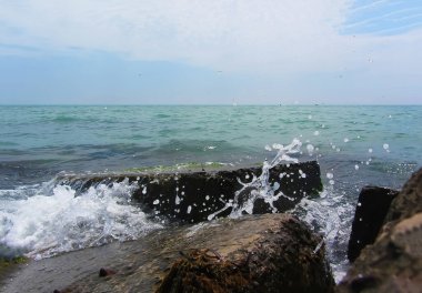 Görüntü: Dalga yeşil alglerle kaplı iskelede kare bir kayanın üzerinden geçiyor. Zümrüt renkli deniz kıyıdaki beton levhaya çarpıyor. Tatilde taze deniz sörfü