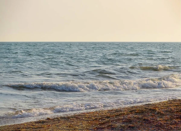 Güneşli bir yaz gününde gün batımında plaj. Sahilde deniz günbatımı manzarası. Deniz dalgası gün batımı renginde karaya çıktı. Batan güneşin ılık, yumuşak renklerinde. Dalgalar denize yuvarlanıyor.