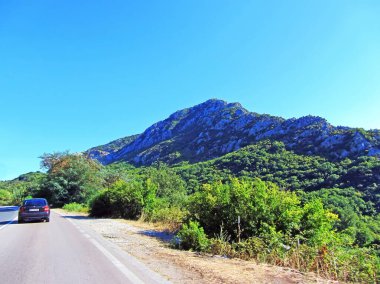 Arka planda bir dağ sırası ve arabası olan bir yol. İtalya 'da bir yaz günü yeşillikle kaplanmış bir orga mcala..