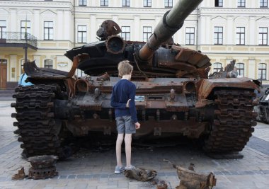 Kiev, Ukraine. 08-02-2022. A skinny boy looks at a burnt-out Russian tank during the Russian-Ukrainian conflict. The remains of a rusty military vehicle. Destroyed and burned tank of Russian invaders.