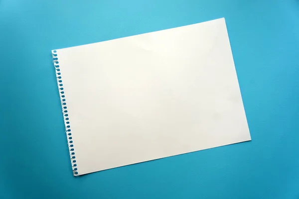 Blank sheet of paper space for design and lettering on a beautiful blue background. A sheet of perforated paper torn from a notepad rests obliquely on the surface. Square sheet of paper copyspace